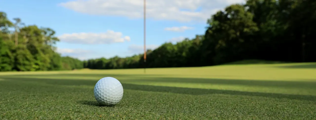 A golf ball on the green with the flag behind