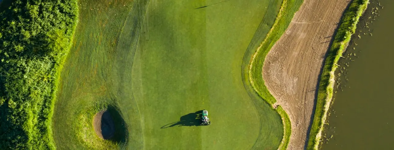 Aerial view of a green beside a lake with a mower crossing it