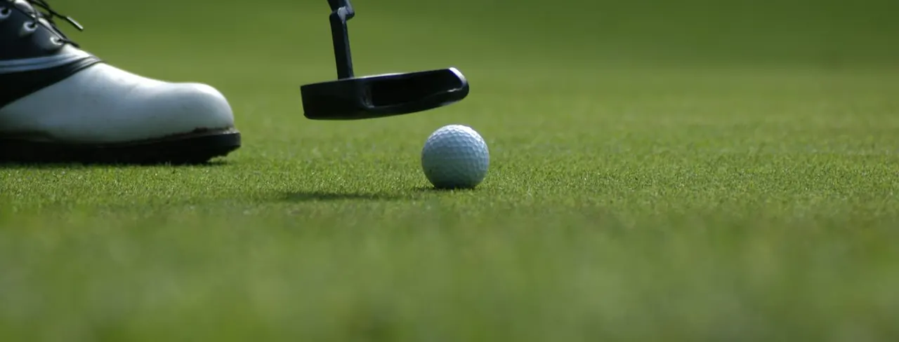 A putter lining up a golf ball on the green