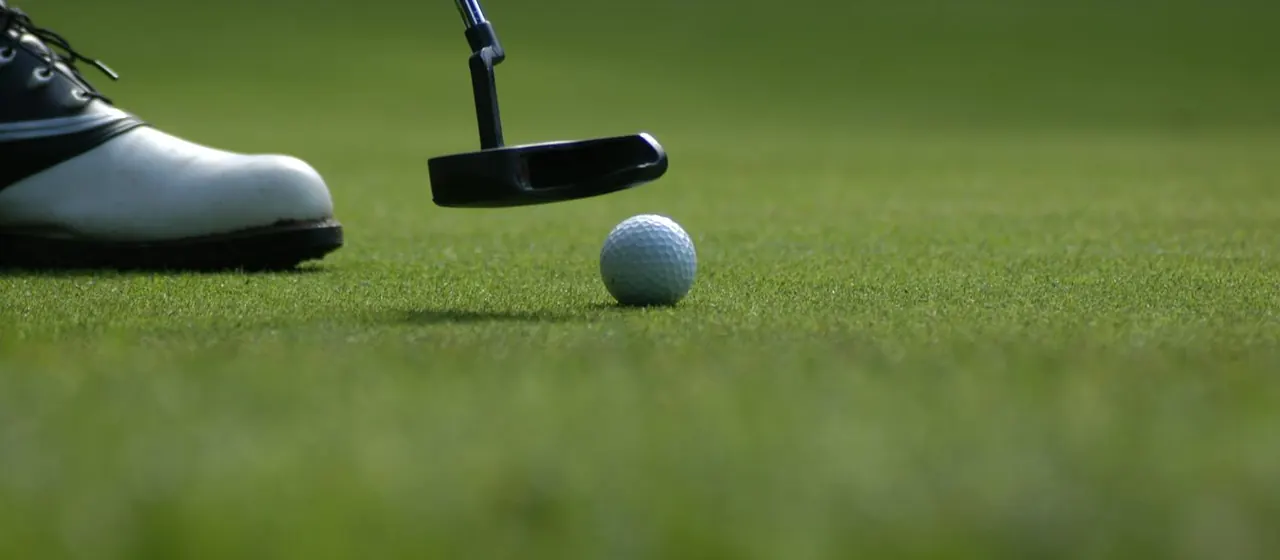 A putter lining up a golf ball on the green