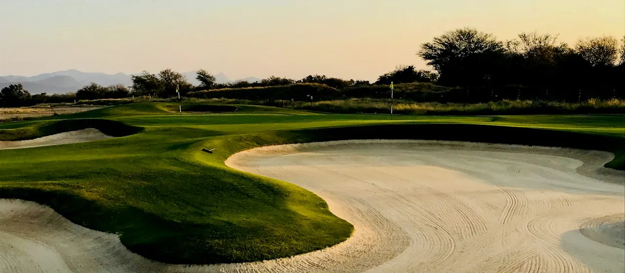 Low evening sun over a raked bunker and green with two flags